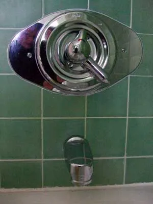 Single-handle chrome shower/tub faucet on a dark green tiled wall, with a short tub spout mounted below.